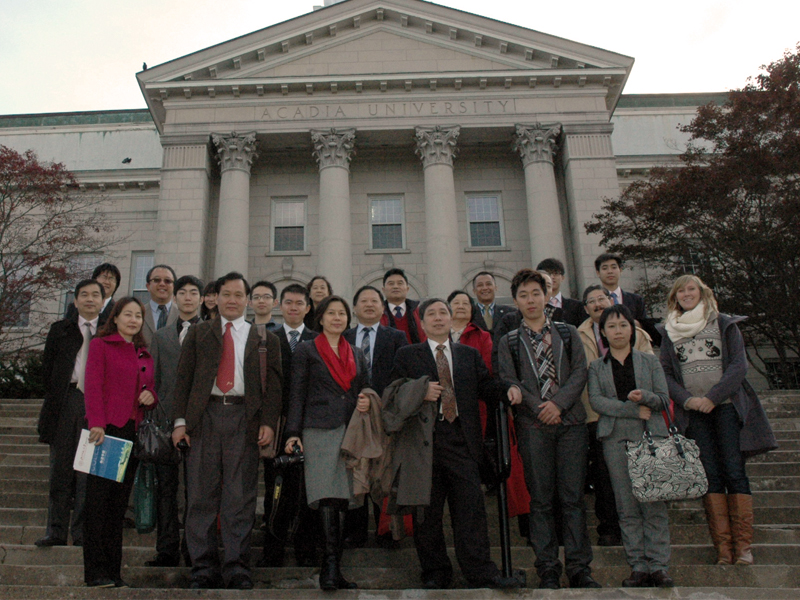 A group of international visitors gather on the steps of University Hall.